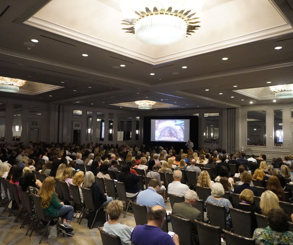 A large group of people in seated in front of a presentation screen in a conference setting